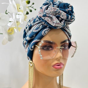Pode incluir: Um turbante azul e branco estampado com um grande n&oacute; no topo. O turbante &eacute; usado por um manequim com longos brincos de corrente dourada e grandes &oacute;culos de sol transparentes adornados com strass.