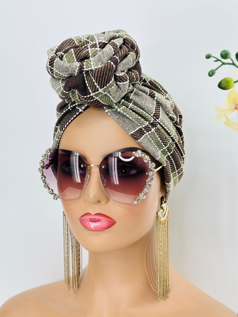 Pode incluir: Um turbante estampado em marrom e verde com um n&oacute; no topo. O turbante &eacute; usado por um manequim com cabelo castanho e que usa &oacute;culos de sol grandes em forma de cora&ccedil;&atilde;o com pedrarias e brincos de corrente dourada.