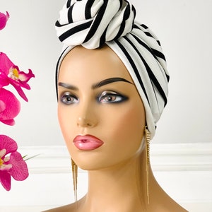 Pode incluir: Um turbante listrado branco e preto com um grande n&oacute; no topo. O turbante &eacute; feito de um tecido macio e el&aacute;stico.