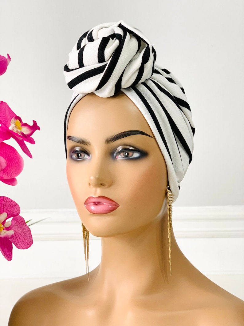 Pode incluir: Um turbante listrado branco e preto com um grande n&oacute; no topo. O turbante &eacute; feito de um tecido macio e el&aacute;stico.