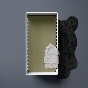 May include: A white crib with a green mattress and a white blanket inside. A black fuzzy rug is on the floor next to the crib.