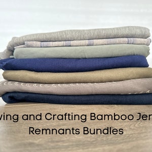 K&ouml;nnte beinhalten: Ein Stapel Stoffreste in verschiedenen Graut&ouml;nen, Gr&uuml;n, Blau, Braun und Beige. Der Stoff wird als "Sewing and Crafting Bamboo Jersey Remnants Bundles" beschrieben.