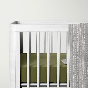 Può includere: Un lettino in legno bianco con un lenzuolo con angoli elastici verde e una coperta con motivo grigio e bianco.