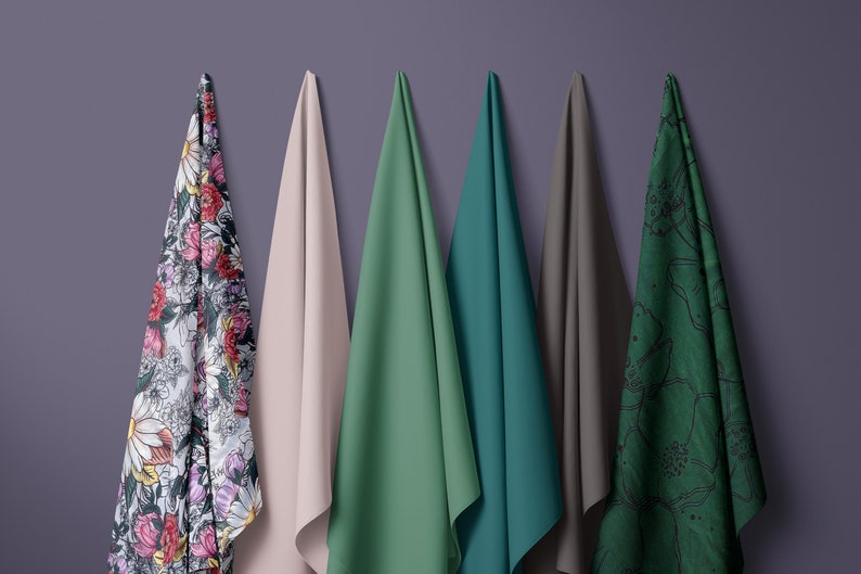 Puede incluir: Cinco muestras de tela colgadas en una pared morada. Las muestras son de varios colores y patrones, incluyendo floral, rosa s&oacute;lido, verde s&oacute;lido, verde azulado s&oacute;lido y un patr&oacute;n floral verde.