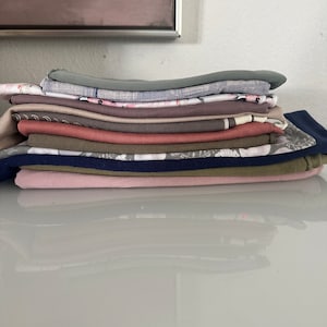 May include: A stack of fabric scraps in various colors and patterns, including pink, brown, green, and blue.