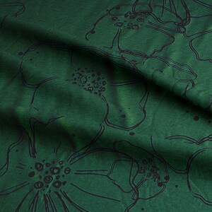 Puede incluir: Tela verde con un patr&oacute;n floral negro. La tela est&aacute; doblada y tiene una superficie texturizada.