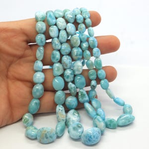 May include: A strand of light blue and white Larimar gemstone beads. The beads are smooth and oval-shaped.