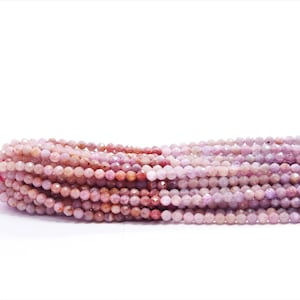 May include: A strand of pink and purple gemstone beads. The beads are faceted and have a slightly irregular shape. The beads are strung on a pink thread.