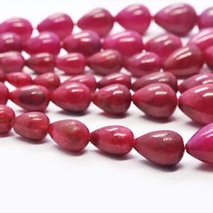 Könnte beinhalten: Eine Kette aus rosafarbenen tropfenförmigen Perlen. Die Perlen sind aus einem glatten, polierten Material gefertigt und haben einen leichten Glanz.