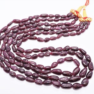 May include: A strand of deep red ruby gemstone beads, each bead is oval shaped and polished. The beads are strung on a cord with a tassel at the end.