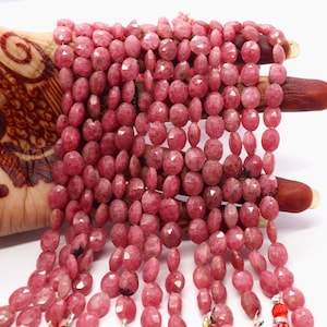 May include: A strand of pink gemstone beads, faceted and oval shaped. The beads are strung on a silver wire and have a tassel at the end.