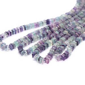May include: A strand of multi-colored gemstone beads. The beads are faceted and have a square shape. The colors of the beads are purple, green, and blue.
