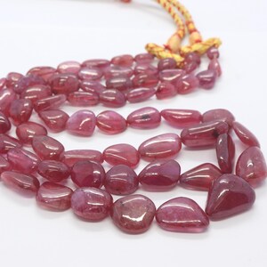 May include: A strand of pink gemstone beads, strung on a yellow cord. The beads are smooth and have a slightly irregular shape.