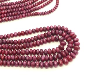 May include: Strands of deep red gemstone beads, varying in size, against a white background. The beads have a polished, rounded shape, and the color is a rich, dark red. The arrangement suggests jewelry making or crafting.