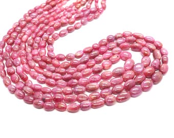 May include: A collection of oval-shaped, polished pink gemstones, likely beads, arranged in multiple strands. The beads have a smooth, glossy surface and vary slightly in shade, creating a rich, textured appearance. The background is plain white.