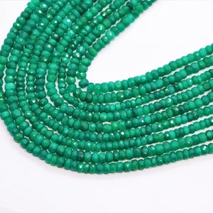 Puede incluir: Una hebra de cuentas de piedras preciosas verdes, probablemente esmeralda o peridoto, con una forma facetada ligeramente irregular. Las cuentas están enhebradas en un hilo transparente y están dispuestas en un patrón suelto y fluido.