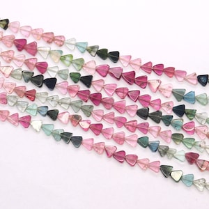 May include: A strand of multi-coloured triangle shaped gemstone beads. The beads are a mix of pink, green, blue, and black.