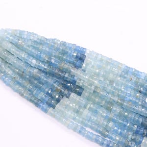 May include: Strands of aquamarine gemstone beads in varying shades of blue. The beads are small, square-cut, and strung together, creating a textured, shimmering effect. A light blue cord is attached to the top of the strands.