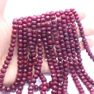 May include: A strand of deep red faceted gemstone beads. The beads are round and have a smooth, polished finish.