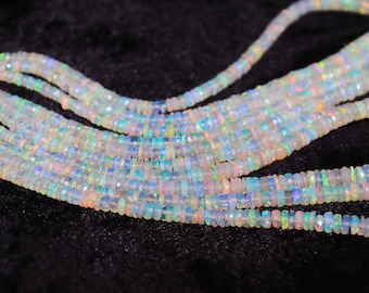 May include: Strands of iridescent opal beads, displaying a spectrum of colors including blue, green, and pink. The beads are small, rectangular, and strung together, creating a shimmering effect against a dark background. Ideal for jewelry making.