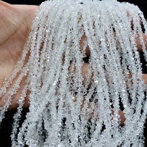 K&ouml;nnte beinhalten: Eine Str&auml;hne aus klaren, facettierten Kristallperlen. Die Perlen sind klein und haben eine diamantartige Form. Die Str&auml;hne ist lang und liegt auf einer Hand.