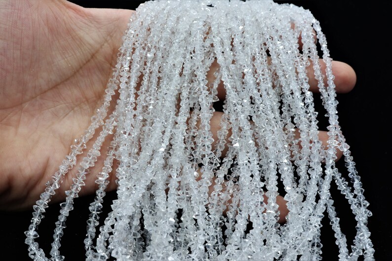 K&ouml;nnte beinhalten: Eine Str&auml;hne aus klaren, facettierten Kristallperlen. Die Perlen sind klein und haben eine diamantartige Form. Die Str&auml;hne ist lang und liegt auf einer Hand.