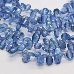 May include: A strand of light blue gemstone beads, each bead is faceted and has a slightly oval shape.