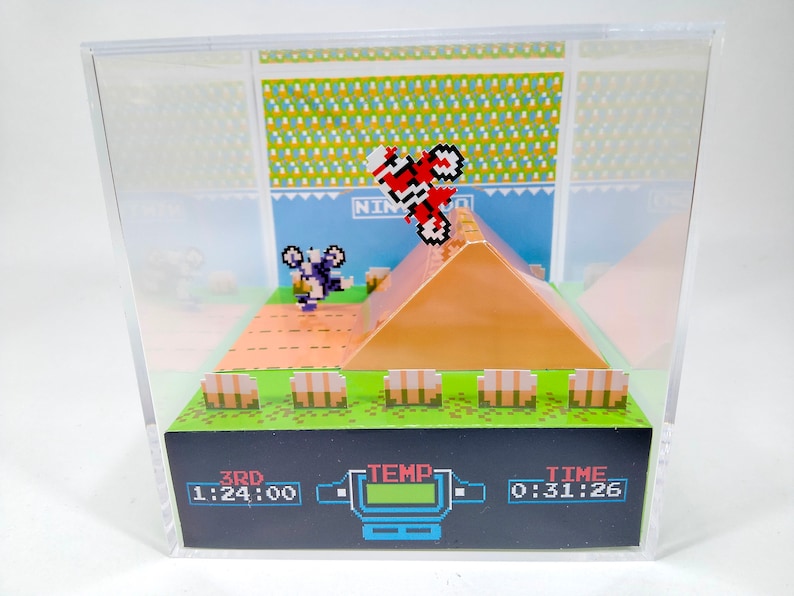 May include: A 3D diorama of a vintage video game, featuring a red motorcycle jumping over a dirt ramp. The diorama includes a pixelated background with the text "NINJA" and a score display showing "3RD 1:24:00", "TEMP", and "TIME 0:31:26".