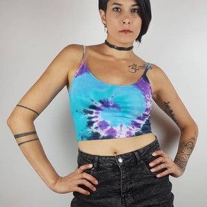 Könnte beinhalten: Eine Frau trägt ein tie-dye Crop-Top in den Farben Blau, Lila und Weiß. Sie trägt auch einen schwarzen Jeans-Minirock.
