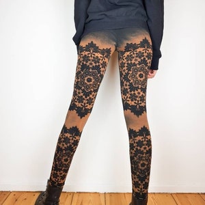 Peut inclure: Leggings noirs avec un motif de dentelle marron et noir. Les leggings sont portés par une personne debout devant un mur blanc.