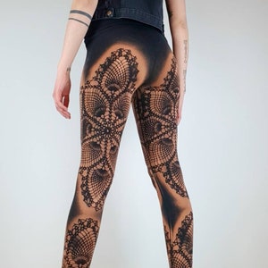 Könnte beinhalten: Schwarze Leggings mit einem bedruckten Spitzenmuster. Die Leggings werden von einer Person mit schwarzen Haaren und einer Jeansweste getragen. Die Person steht auf einem Holzboden.