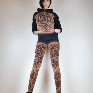 Pu&ograve; includere: Una felpa nera con un grande disegno di mandala sul davanti, abbinata a leggings neri e marroni con un disegno di mandala simile. La modella indossa stivaletti neri alla caviglia.