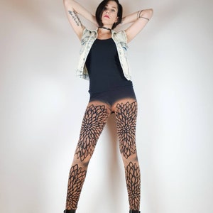Pu&ograve; includere: Una donna indossa una canotta nera, una giacca di jeans blu chiaro e leggings neri con un motivo floreale. Indossa stivaletti neri alla caviglia e ha i capelli tirati indietro.