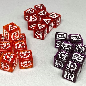 May include: A collection of translucent dice in shades of red and purple. Each die features white symbols and text, including "SHIFT," "SLIDE," and "SPIN." The dice are arranged in small groups, showcasing their design and markings.