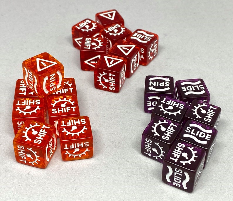 May include: A collection of translucent dice in shades of red and purple. Each die features white symbols and text, including "SHIFT," "SLIDE," and "SPIN." The dice are arranged in small groups, showcasing their design and markings.
