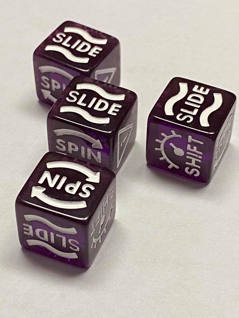 May include: Four translucent purple dice with white text and symbols. Each die features the word "SLIDE" and other action words like "SPIN" and "SHIFT". The dice are arranged on a white surface.