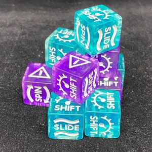 May include: A collection of translucent dice in shades of teal and purple. Each die features the words "SHIFT", "SPIN", and "SLIDE" in white, along with a gear symbol and a warning symbol. The dice are stacked on a dark surface.