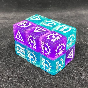 May include: A cube made of nine translucent dice, each with different symbols and the word "SHIFT". The dice are purple and teal, with white graphics. Symbols include a gear, an exclamation point, and a curved arrow. The cube is on a dark surface.