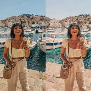 Op de afbeelding: Een vrouw draagt een geel bloemetjes crop top en een beige broek en houdt een ijsje vast. Ze staat op een dok met een blauwe en groene watermassa achter haar. Ze draagt een geweven stro tas met een bruine band.