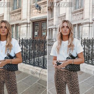 May include: A woman wearing a white t-shirt and leopard print pants stands in front of a building with a black metal fence. She is holding a black studded handbag and a camera.