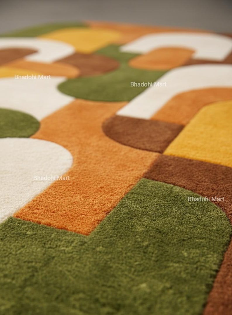 May include: A close-up of a colorful rug with a geometric pattern. The rug features a combination of orange, green, brown, yellow, and white shapes. The text "Bhadohi Mart" is visible in several places on the rug.