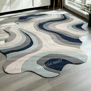 May include: A large, abstract area rug with a flowing, wave-like design. The rug features a blend of cool tones, including shades of blue, gray, and cream. The unique shape and color palette create a modern and artistic aesthetic, suitable for various interior styles.