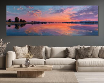 May include: Panoramic canvas art print of a vibrant sunset over a calm lake. The sky transitions from blue to orange and pink, reflecting in the water. Silhouetted trees and distant mountains complete the landscape.