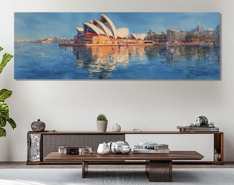 May include: Panoramic canvas art print of the Sydney Opera House, featuring its iconic white sail-like structures against a blue sky. The artwork captures the building's reflection in the water, with city buildings in the background.
