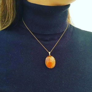 May include: A gold chain necklace with a large oval-shaped pendant featuring a brown gemstone.