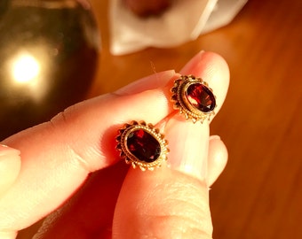 May include: A pair of gold earrings with oval-shaped red gemstones set in a delicate gold filigree design.