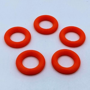 Op de afbeelding: Vijf feloranje rubberen ringen, elk met een rond gat in het midden. De ringen zijn in een cirkel op een wit oppervlak gerangschikt.