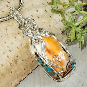 May include: A silver wire wrapped pendant featuring a colorful, orange, white, and turquoise stone. The pendant is on a silver chain.