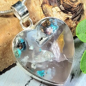 May include: A silver heart-shaped pendant with a clear resin inlay containing various small pieces of turquoise, gold, and other minerals.