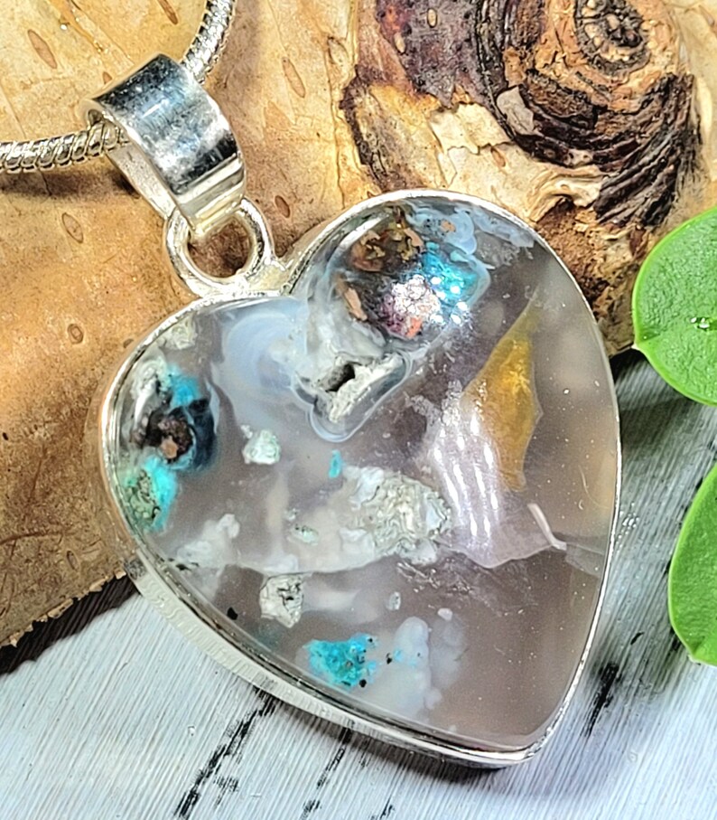 May include: A silver heart-shaped pendant with a clear resin inlay containing various small pieces of turquoise, gold, and other minerals.